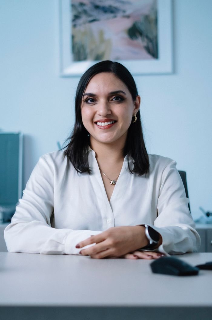 Confident businesswoman in white shirt smiling at her office desk, exuding professionalism and warmth.